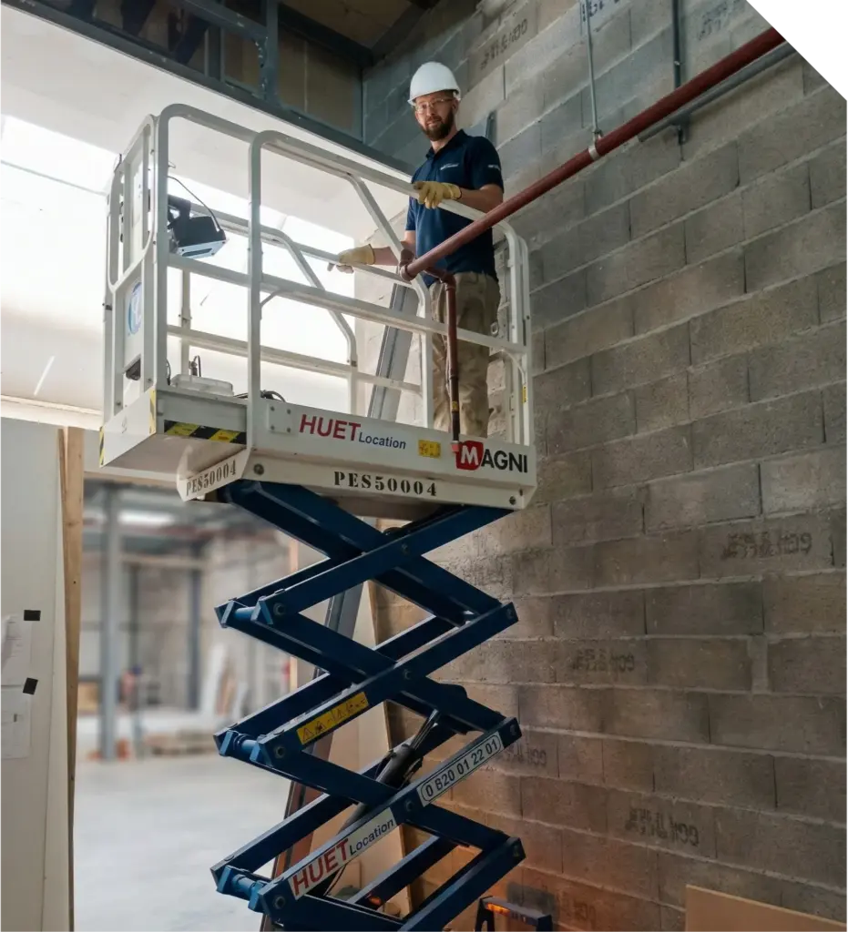 Technicien PROMETAL TMF intervenant en hauteur sur une nacelle élévatrice pour des travaux de métallerie dans un local industriel.